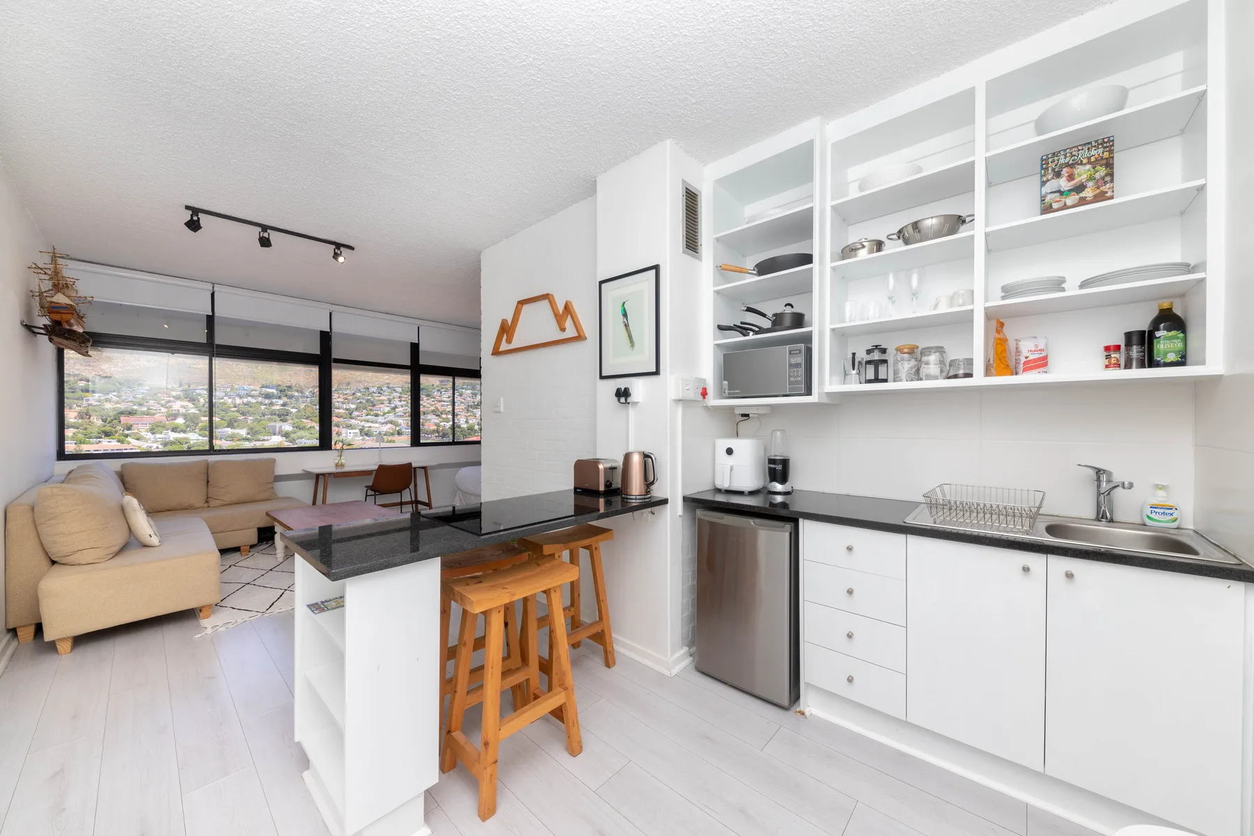 A bright open-plan living area and kitchen with a counter and stools.