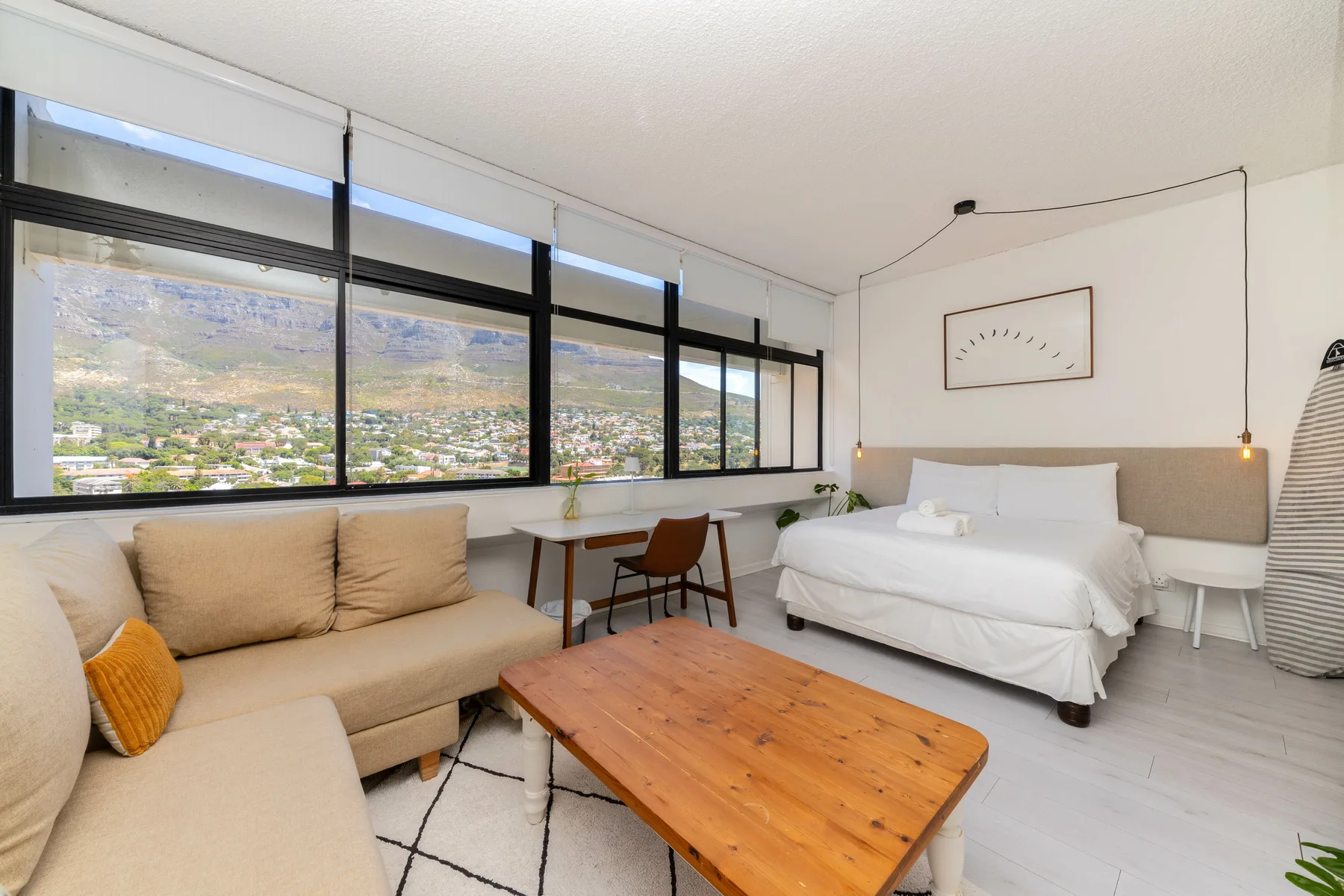 A bright bedroom with a bed, seating, and large windows overlooking the landscape.