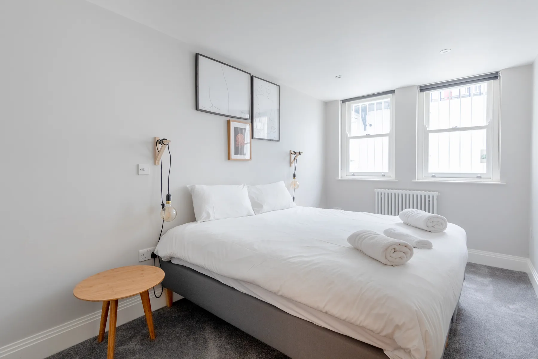 A bright bedroom with a neatly made bed and two windows.