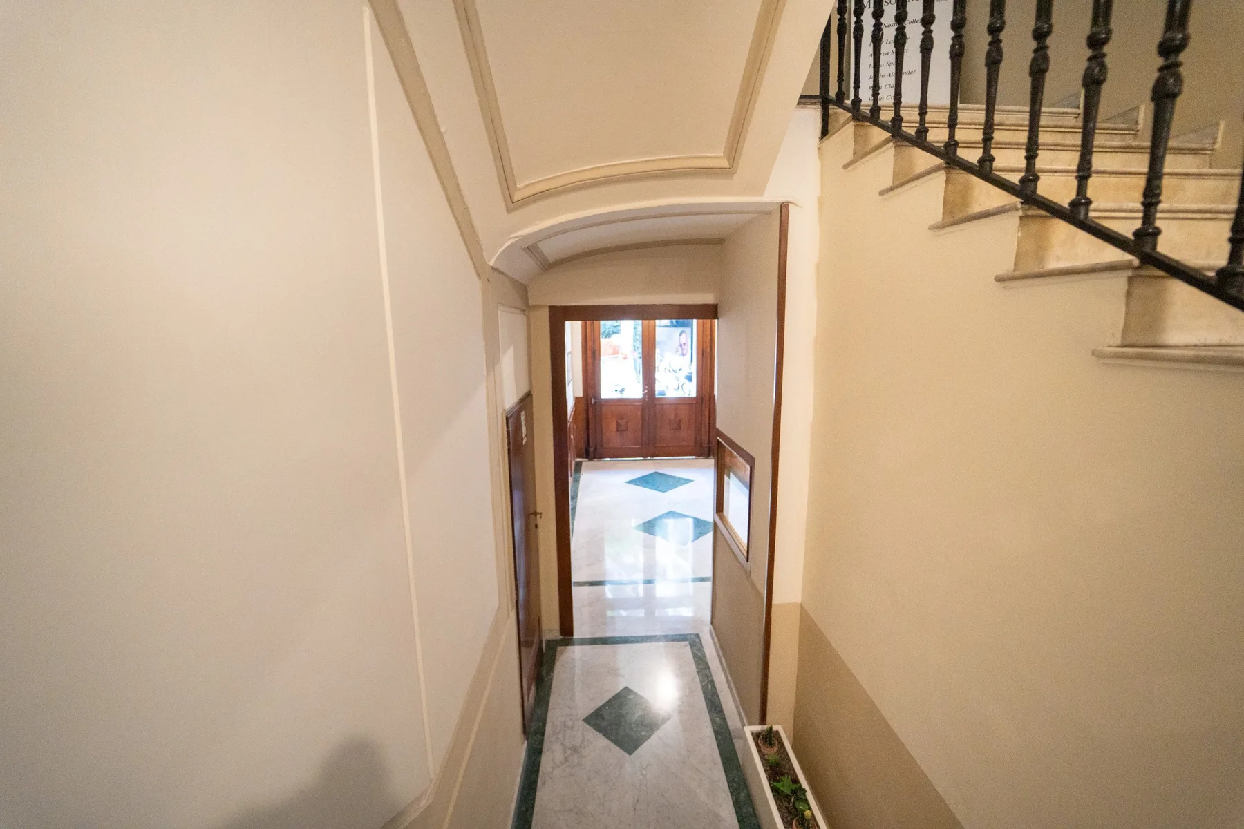 An interior hallway leads toward a wooden door, with a staircase along the right wall.
