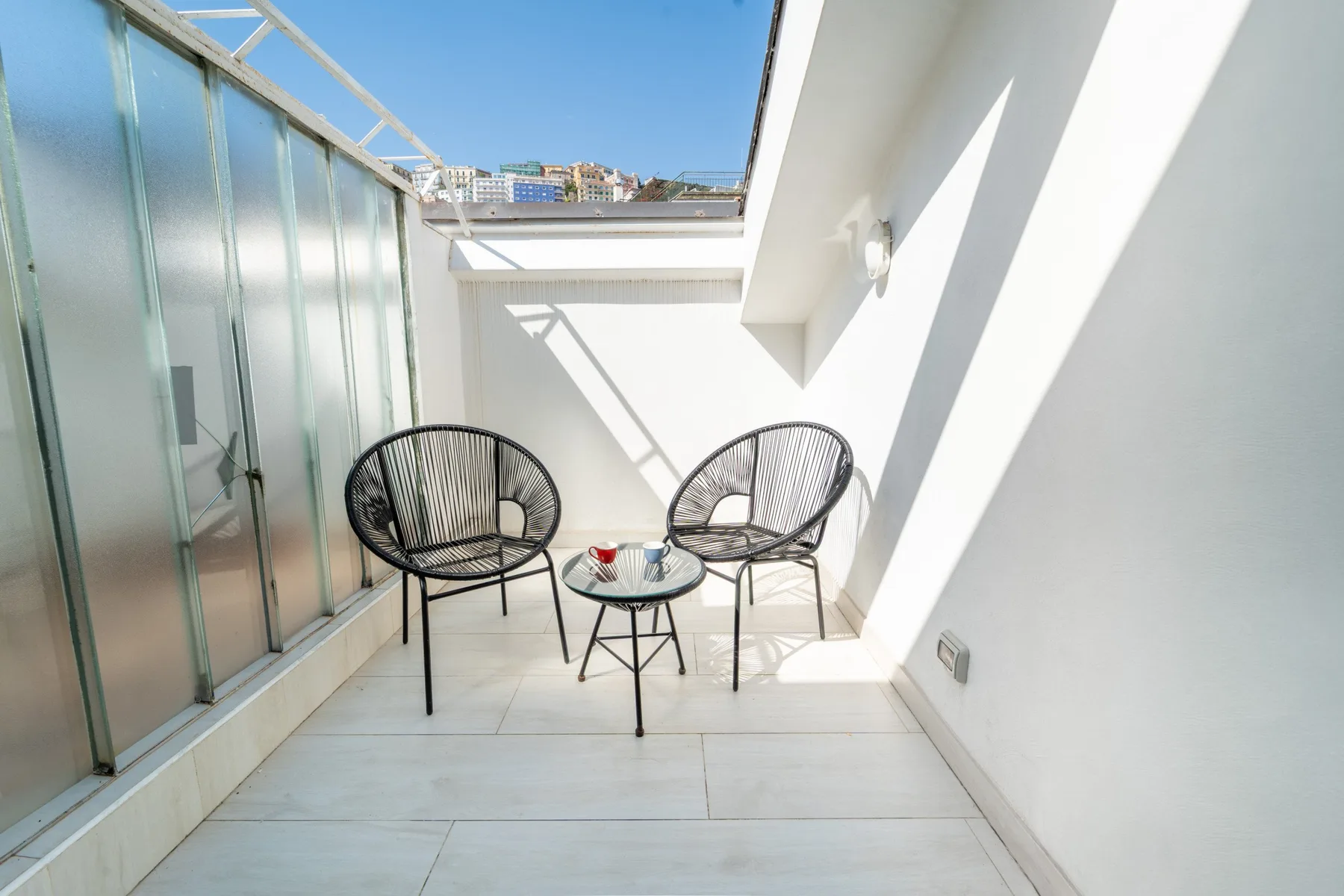 A small outdoor terrace has two chairs and a low table beside glass doors.