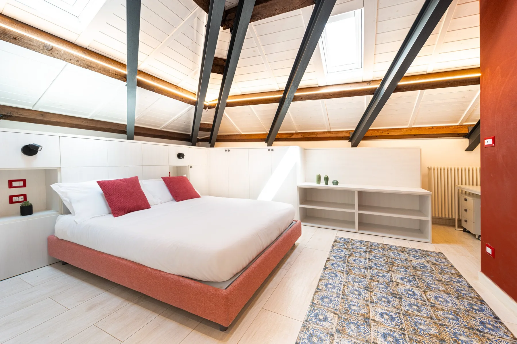 A bright bedroom with a bed, exposed dark beams, and a patterned rug.