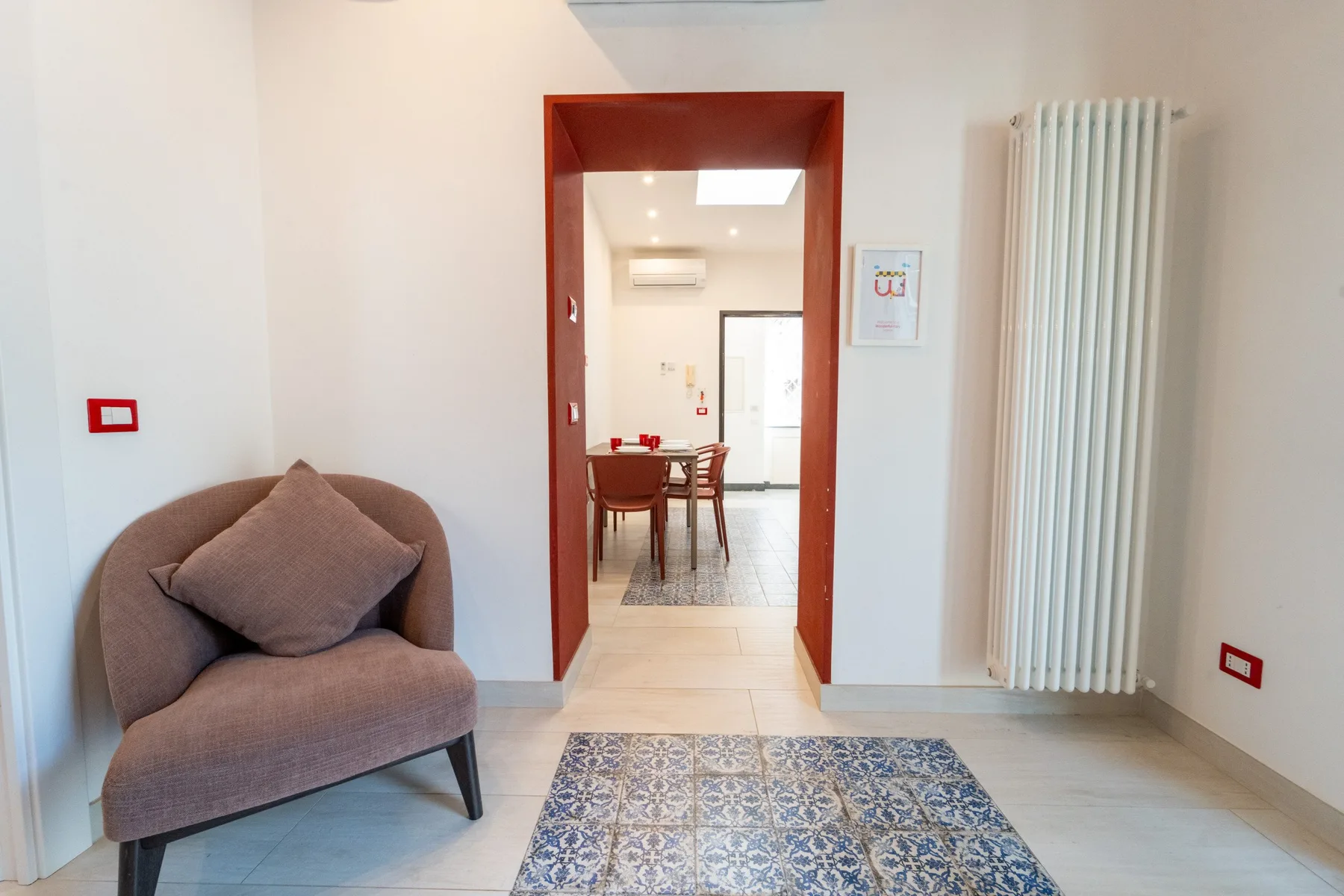 A bright interior hallway opens onto a dining area, with an upholstered seat nearby.