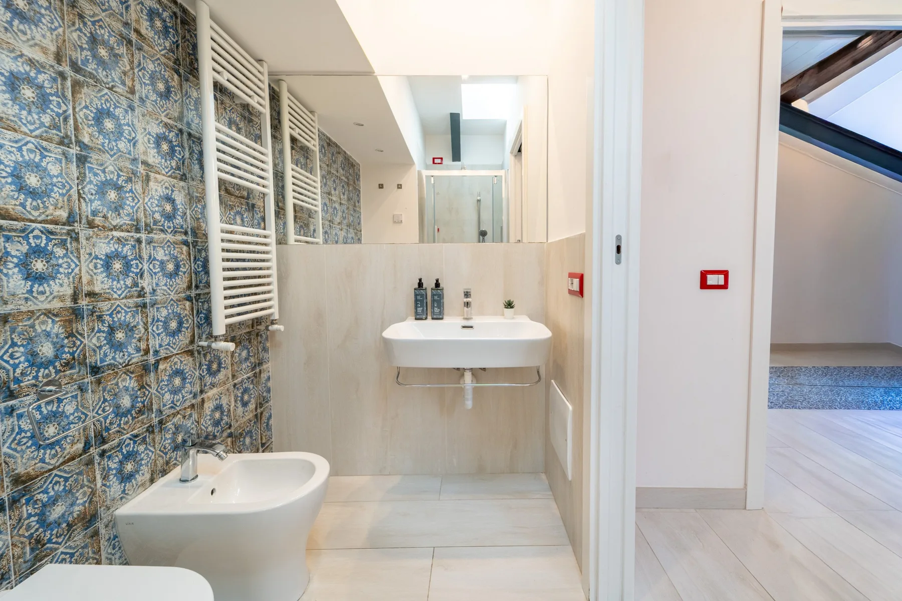 A bright bathroom with a wall-mounted sink and patterned blue tiles.