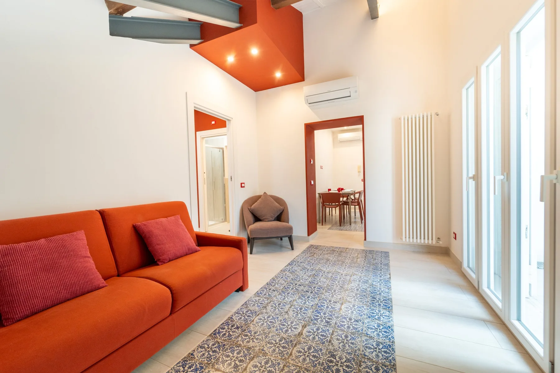A bright living room with orange seating and tall windows.