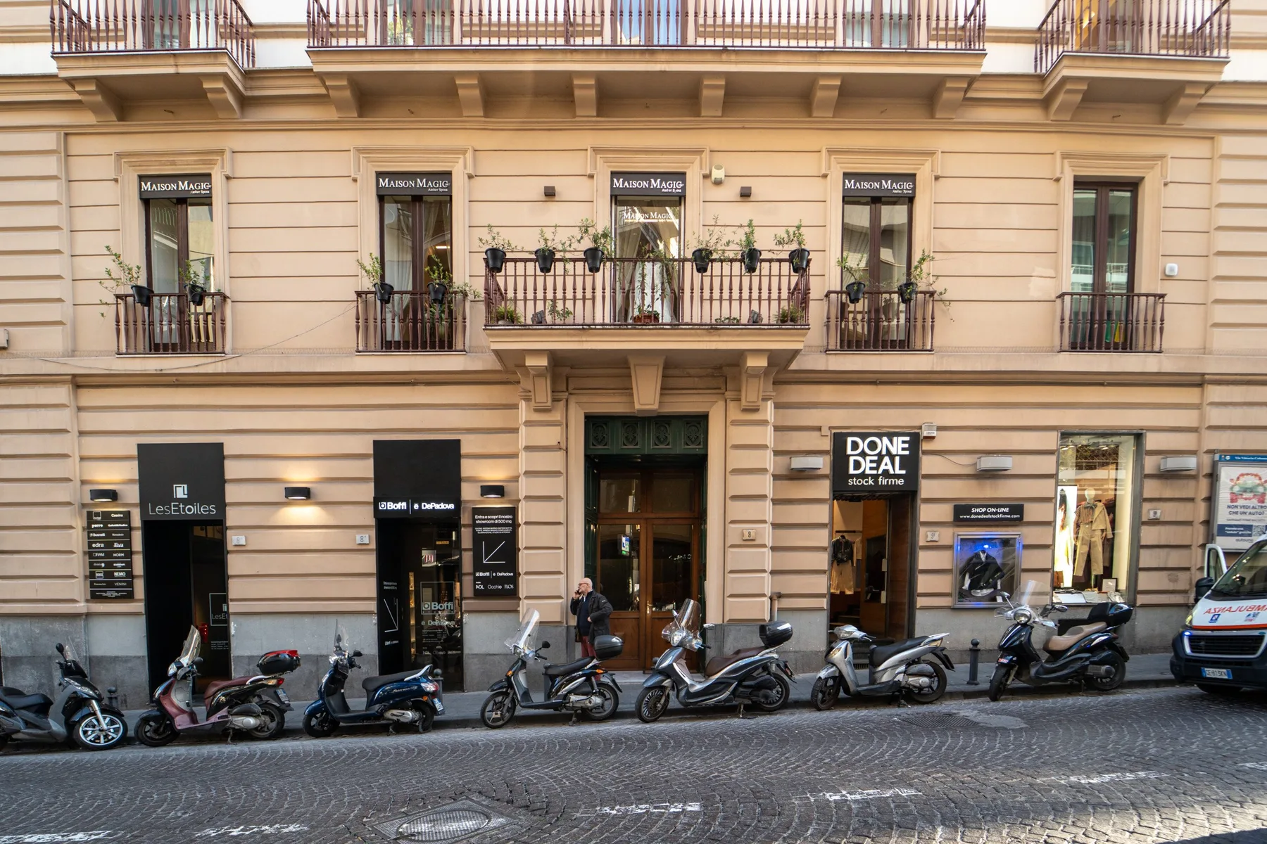 A city street scene with scooters parked along the frontage of a multi-story building.