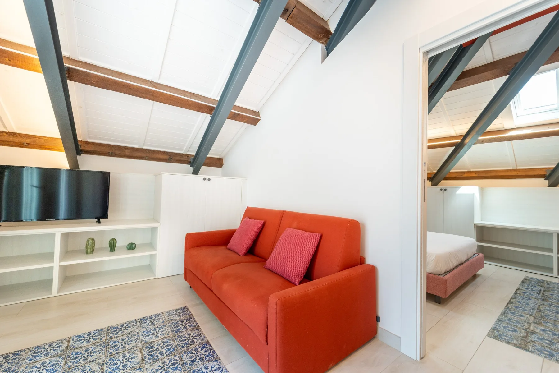 A bright living area with an orange sofa and a wall-mounted television.