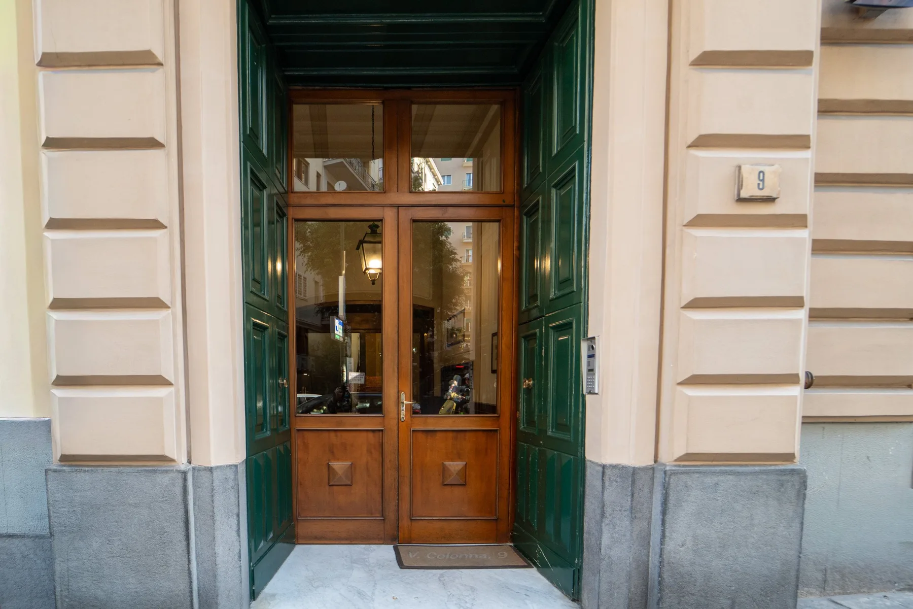 A building entrance with a wooden double door framed by dark green panels.