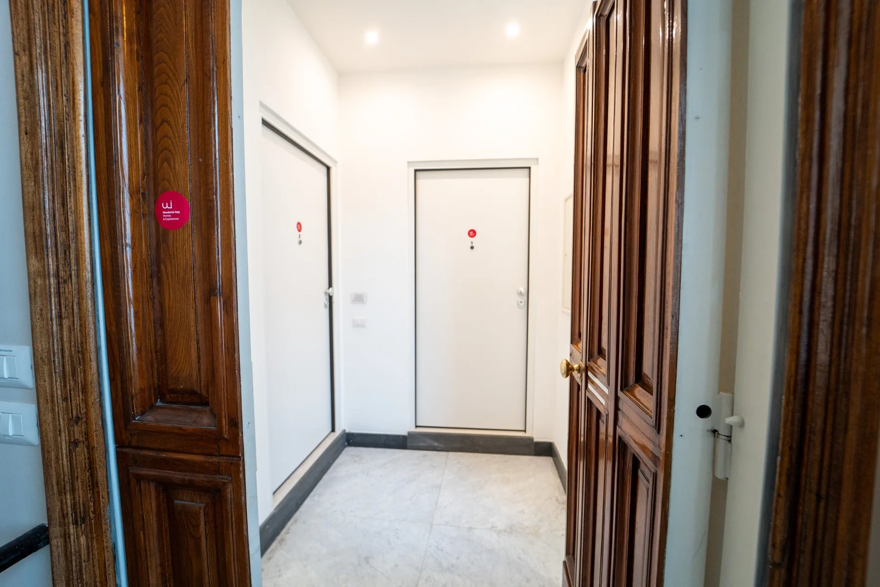 A bright hallway with several closed doors and a tiled floor.