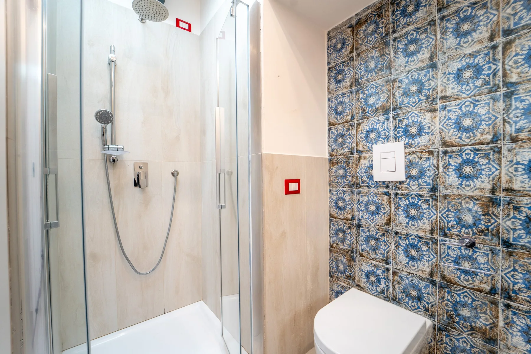 A bathroom with a glass shower and patterned blue wall tiles.
