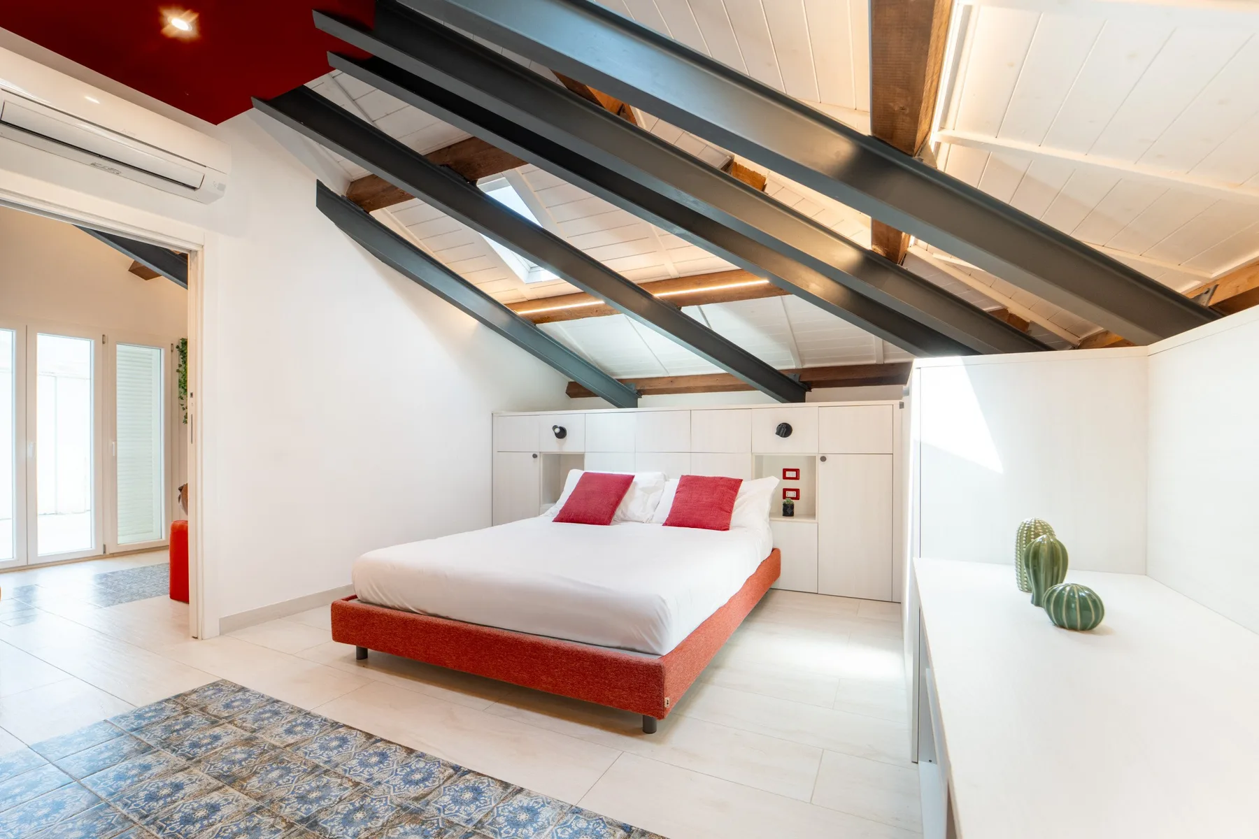 A bright bedroom with a bed beneath exposed ceiling beams.