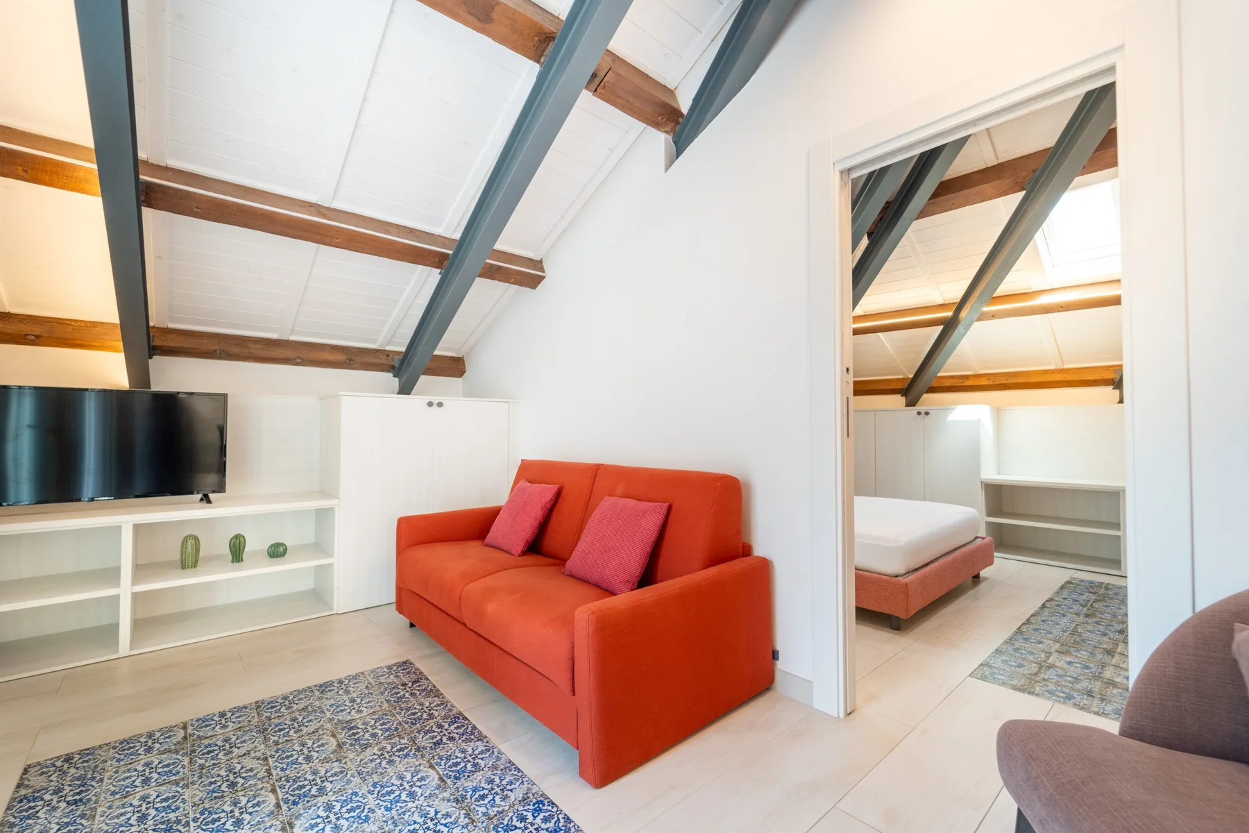 A bright living area has an orange sofa, television, and exposed ceiling beams.