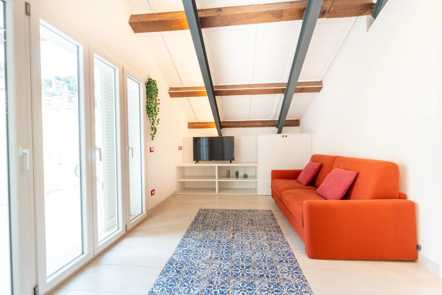 A bright living room with orange seating, a television, and a patterned rug.