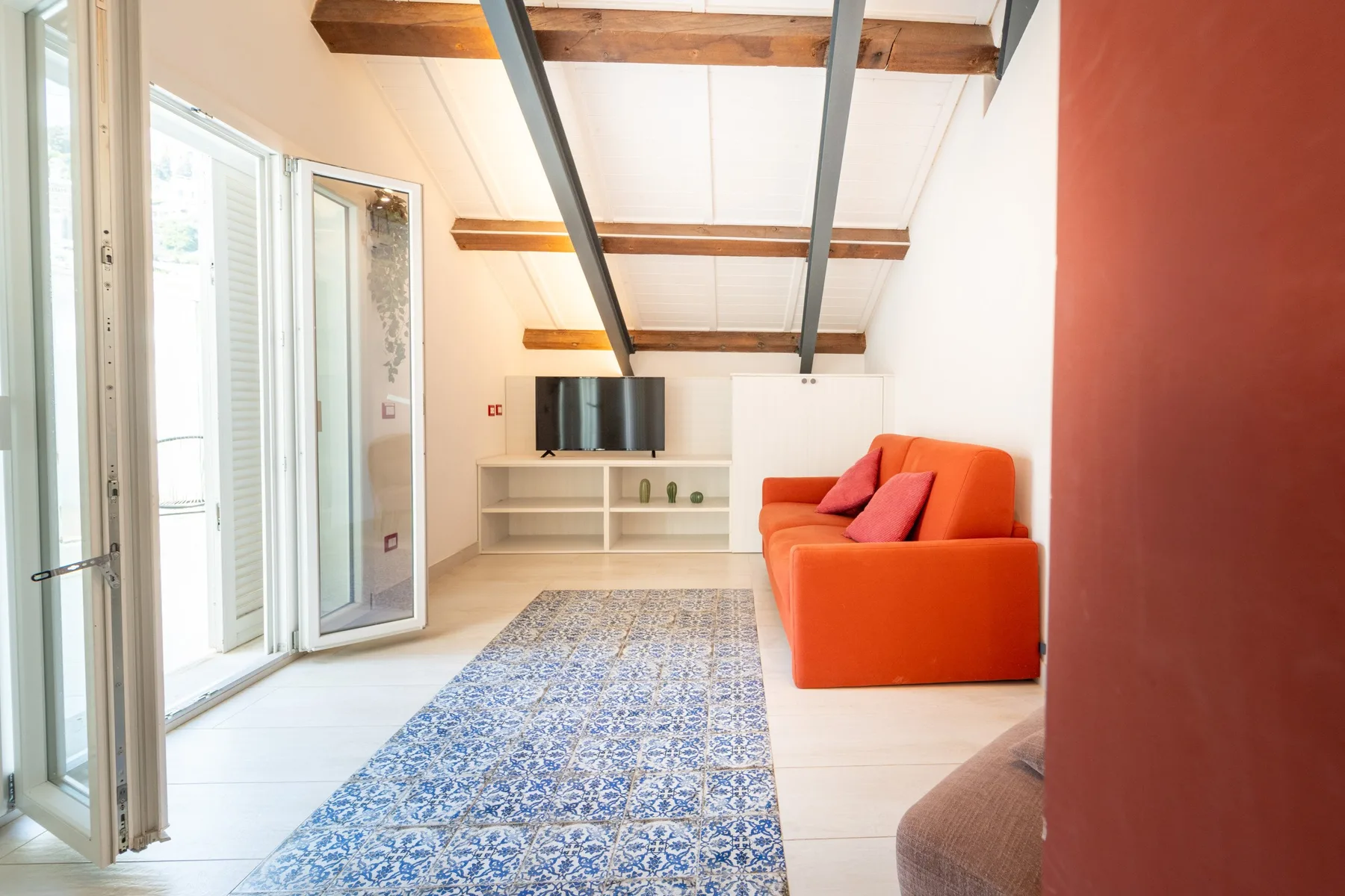 A bright living room with orange seating, a television, and a patterned rug.