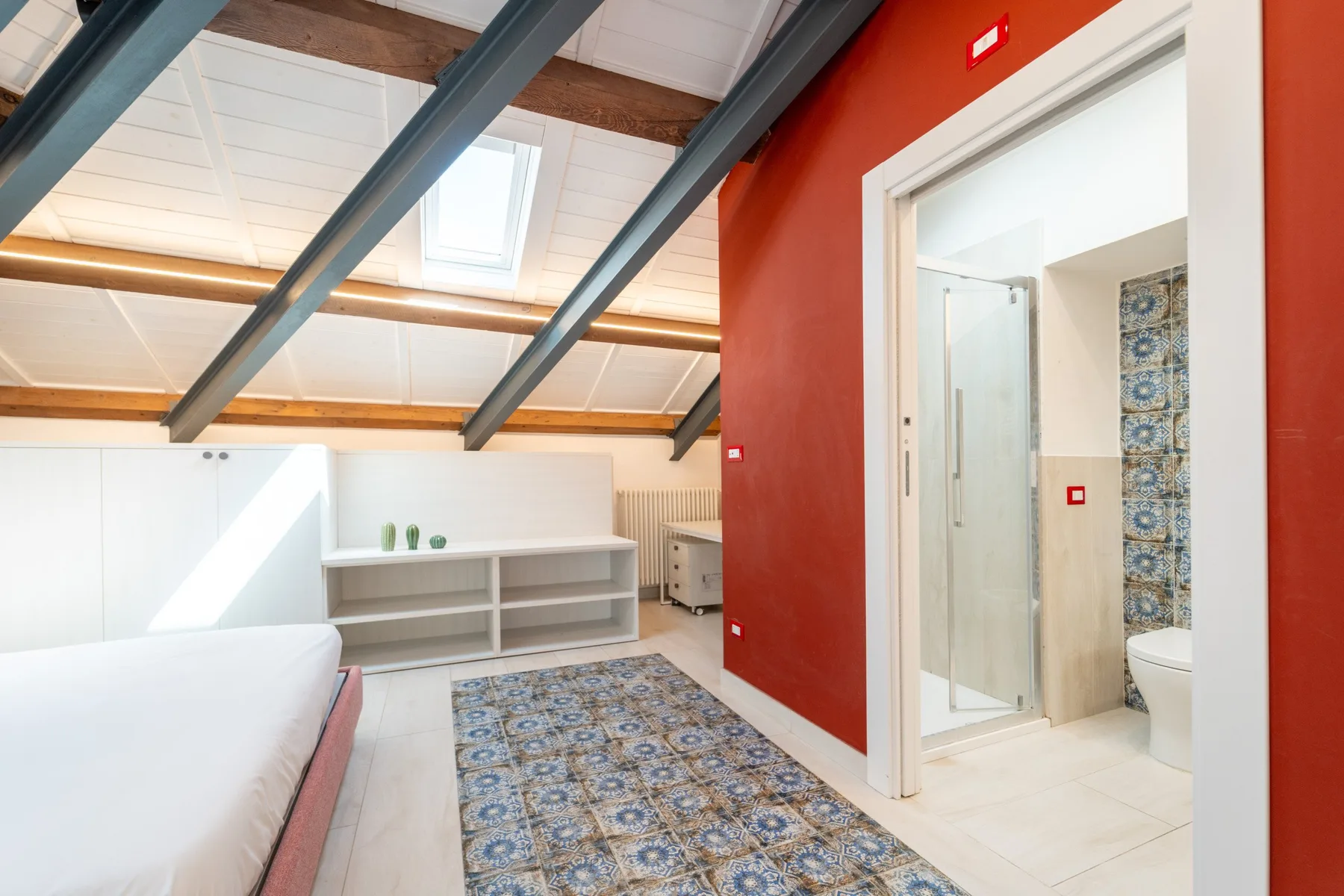 A bright bedroom with a bed, patterned rug, and an open doorway to a bathroom.