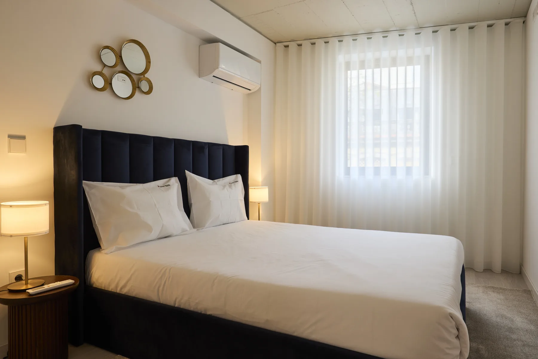 A bedroom with a neatly made bed beside a curtained window.