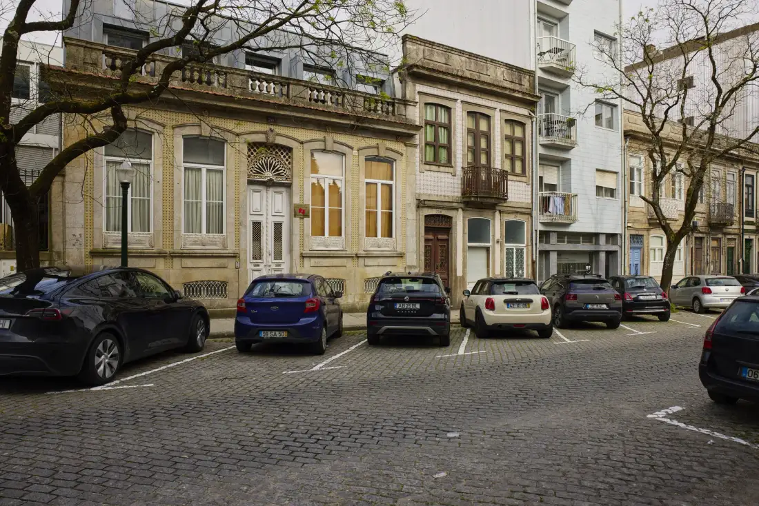 A cobblestone street with parked cars in front of a row of buildings.
