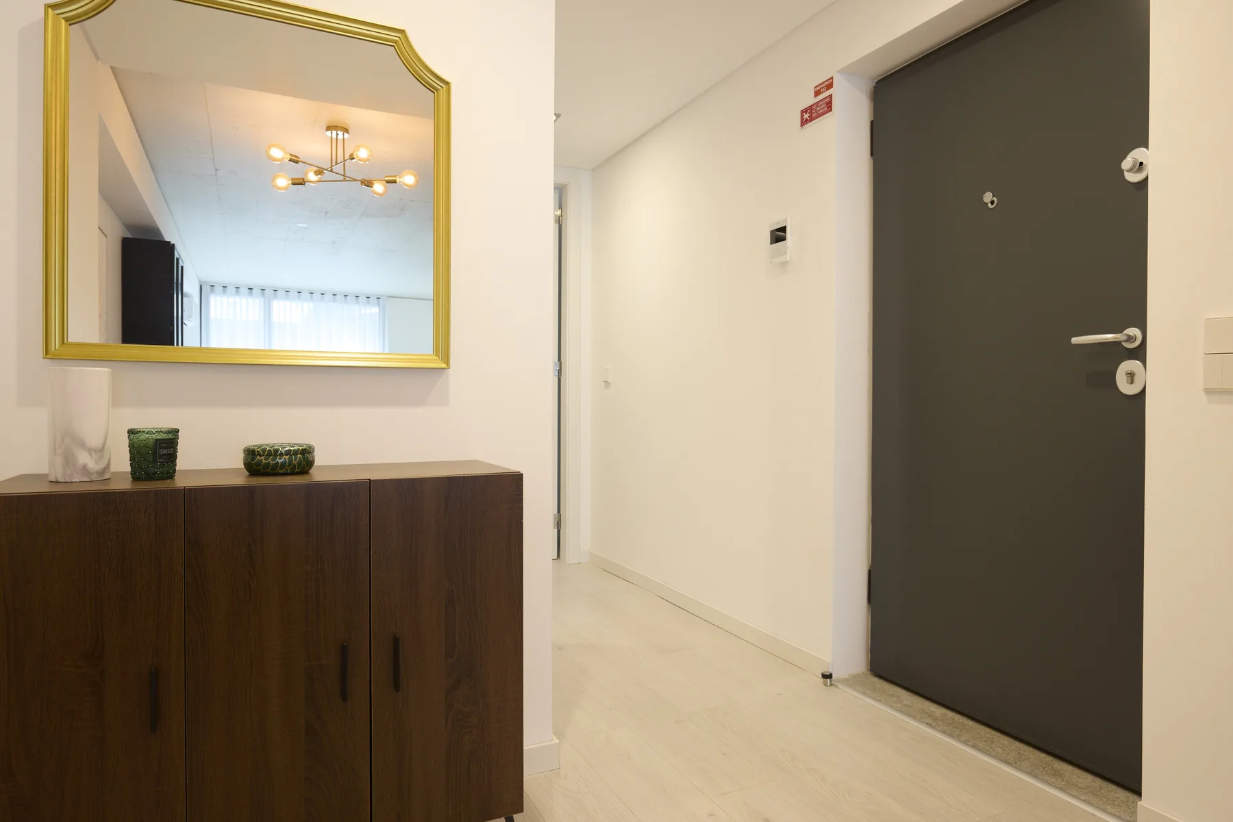 An apartment entry hall with a dark door, wooden cabinet, and gold-framed mirror.