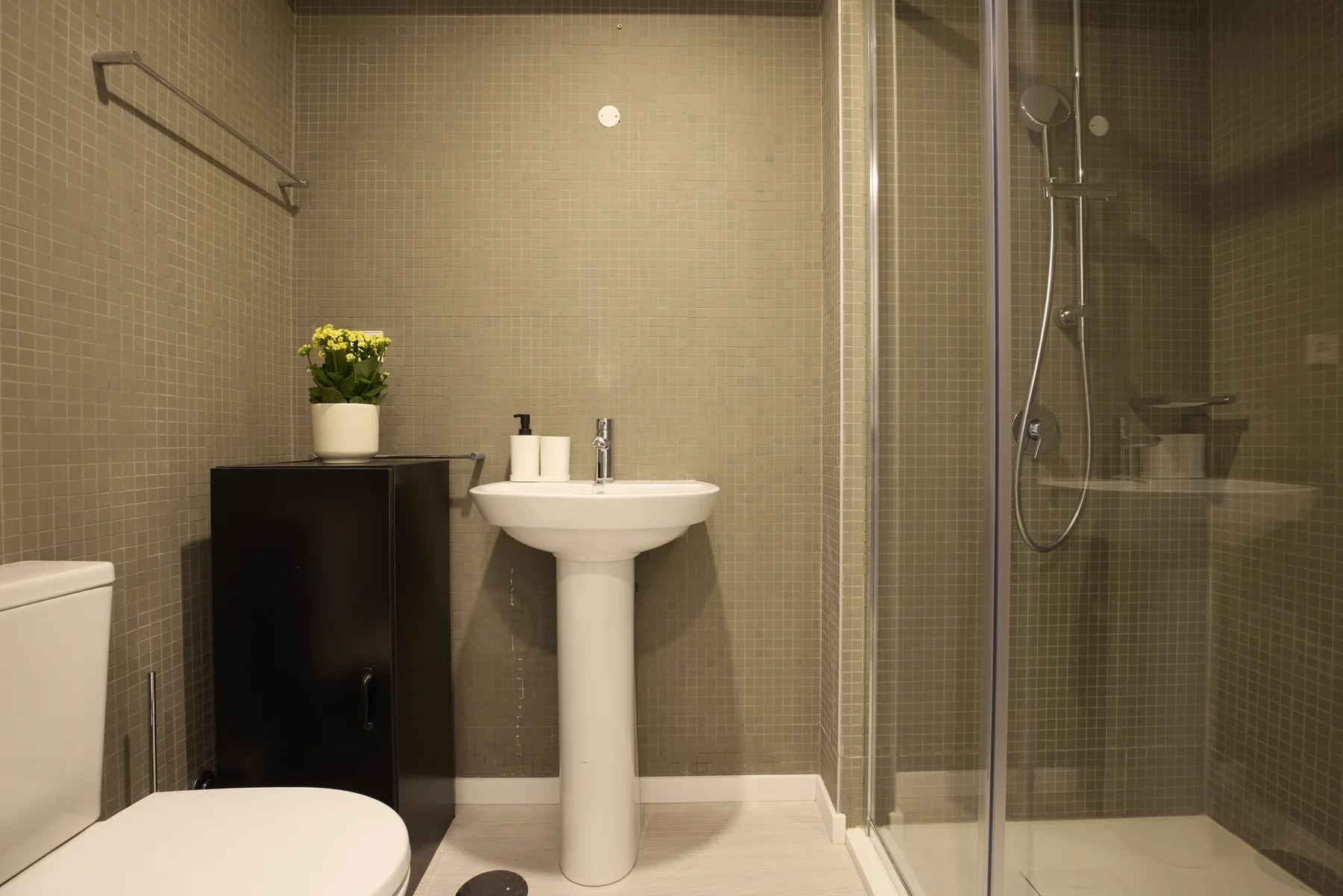 A tiled bathroom with a pedestal sink and glass-enclosed shower.