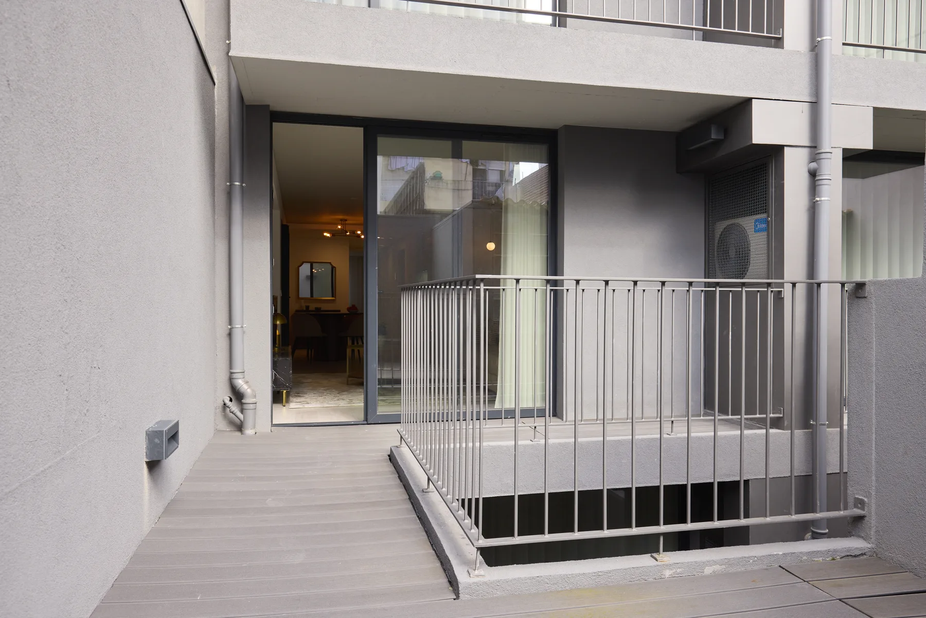 La entrada de un edificio moderno da a una terraza exterior estrecha con barandillas metálicas.