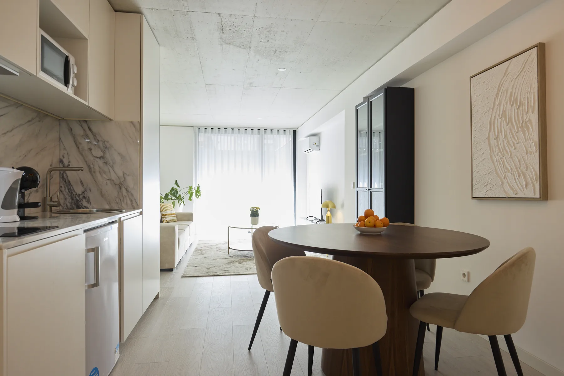 A bright dining area with a round table beside a compact kitchen.