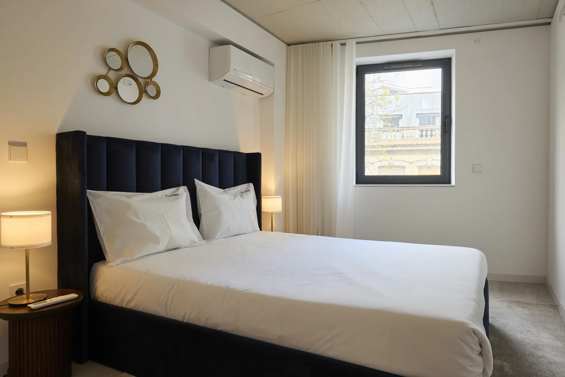 A bedroom with a neatly made bed, bedside lamps, and a window.