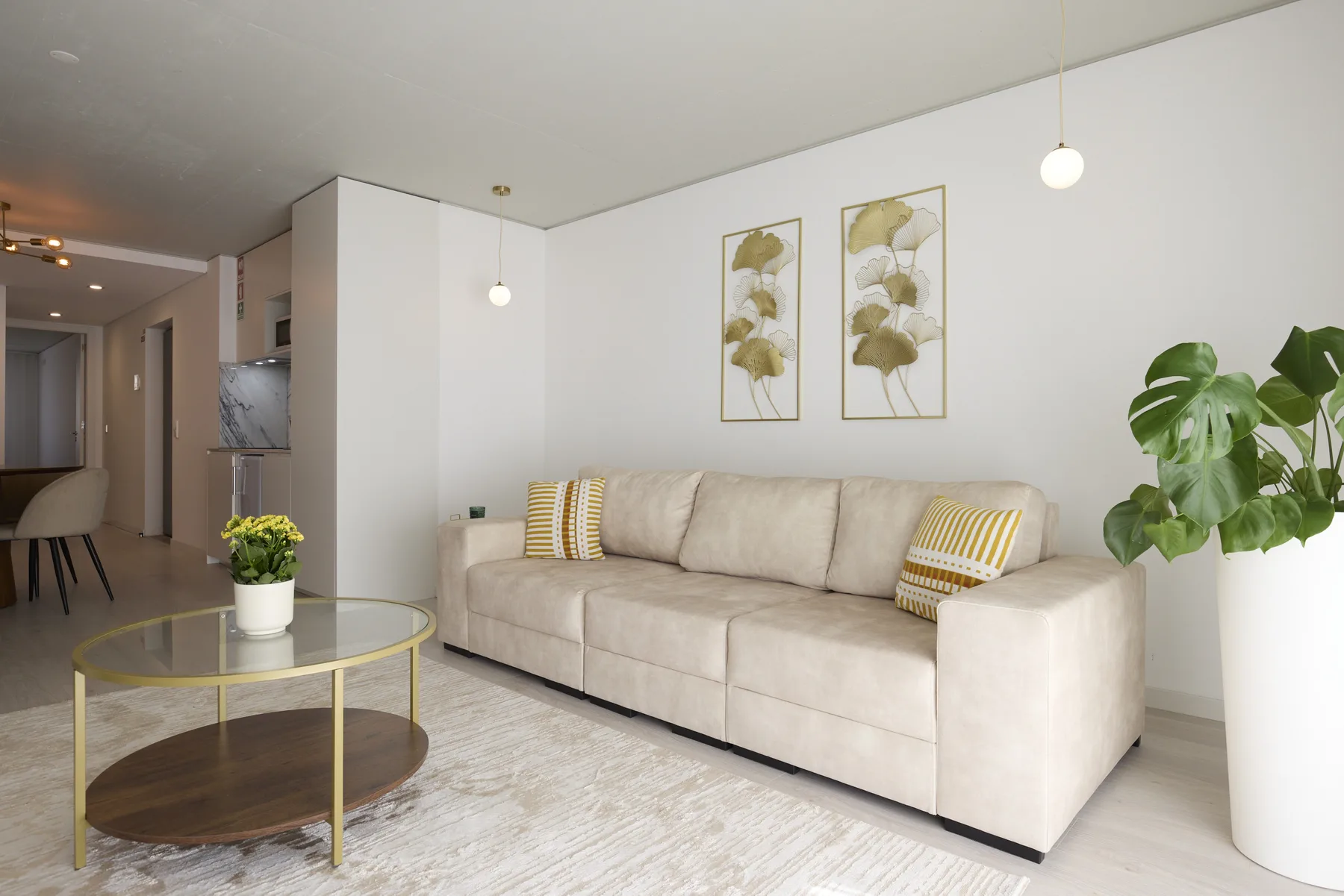 A bright living room with a beige sofa, a glass coffee table, and a potted plant.