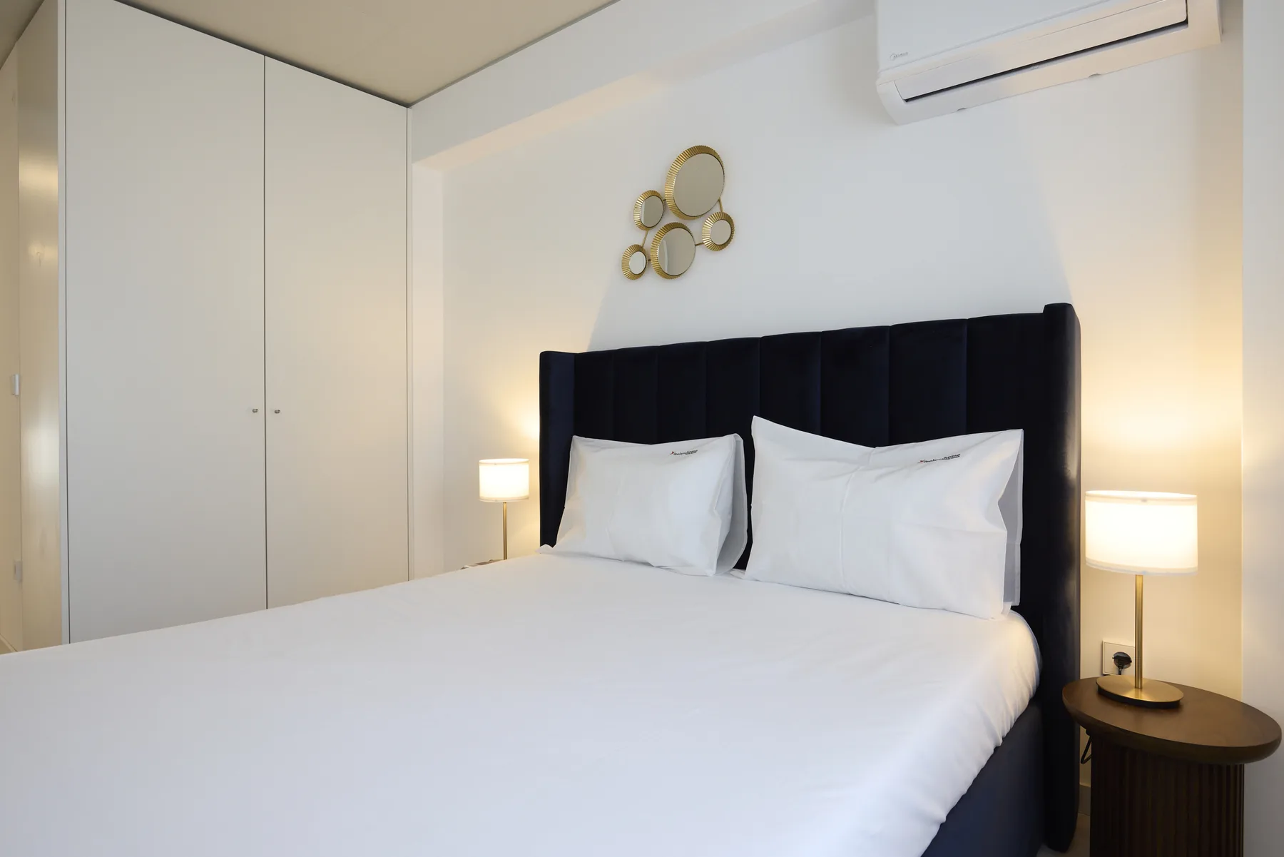 A bedroom with a neatly made bed and black upholstered headboard.