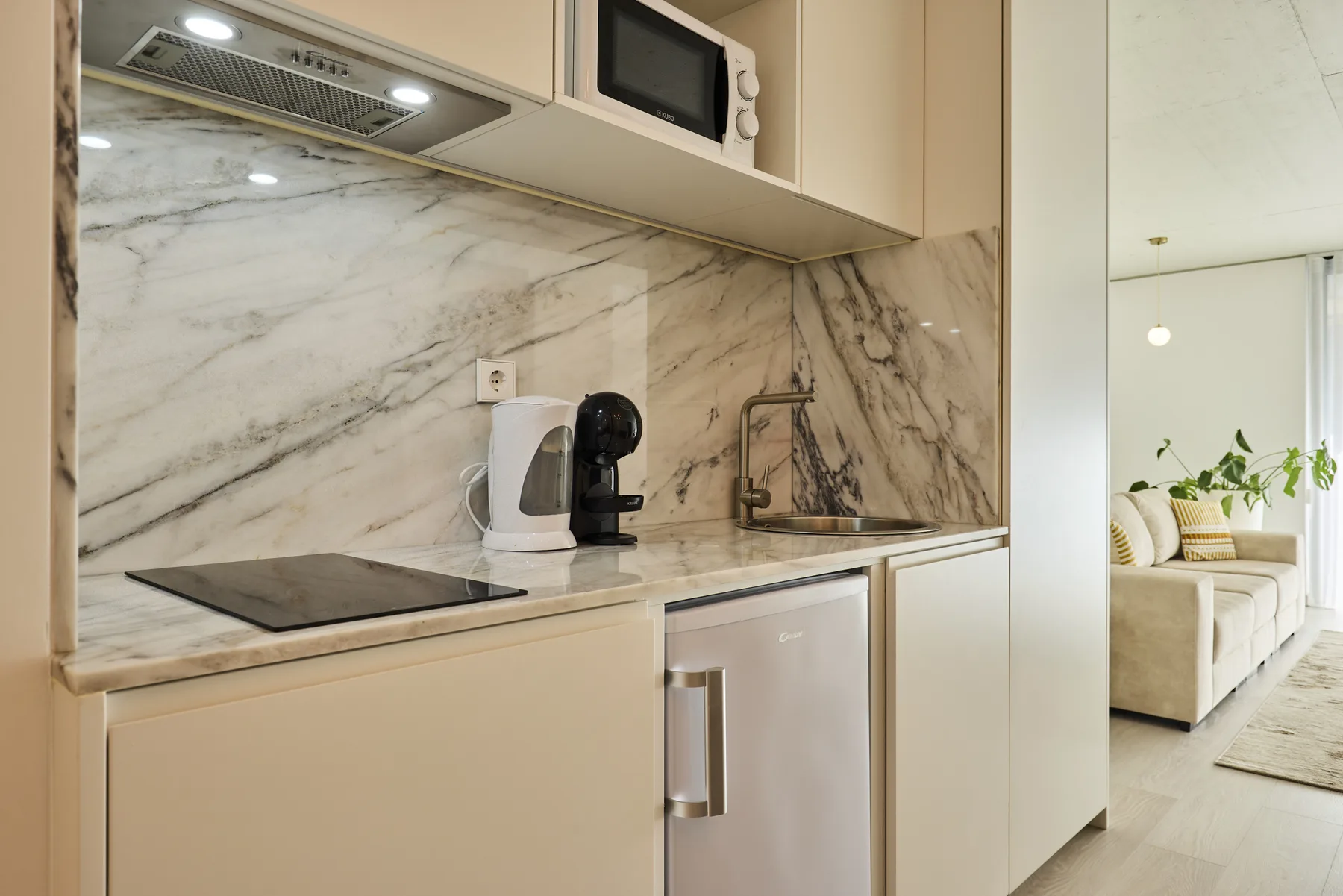 A compact kitchen with a cooktop, countertop appliances, and a sink.