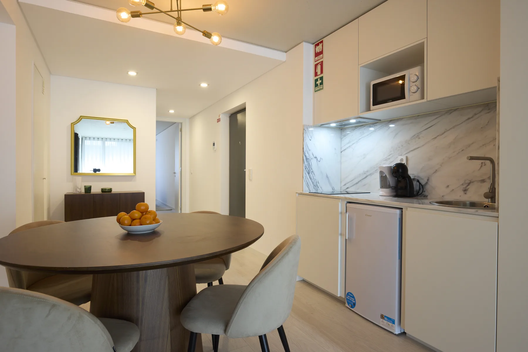 A dining area beside a compact kitchen with light cabinetry and a marble-patterned backsplash.