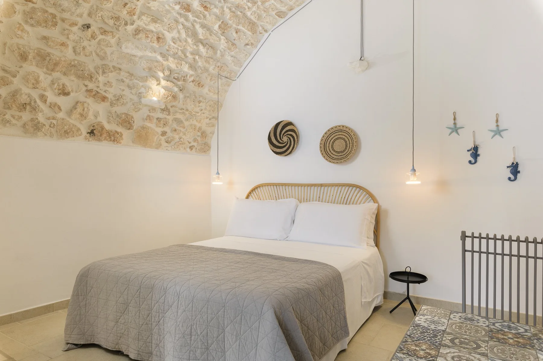 A bedroom with a bed beneath a curved white wall and exposed stonework.