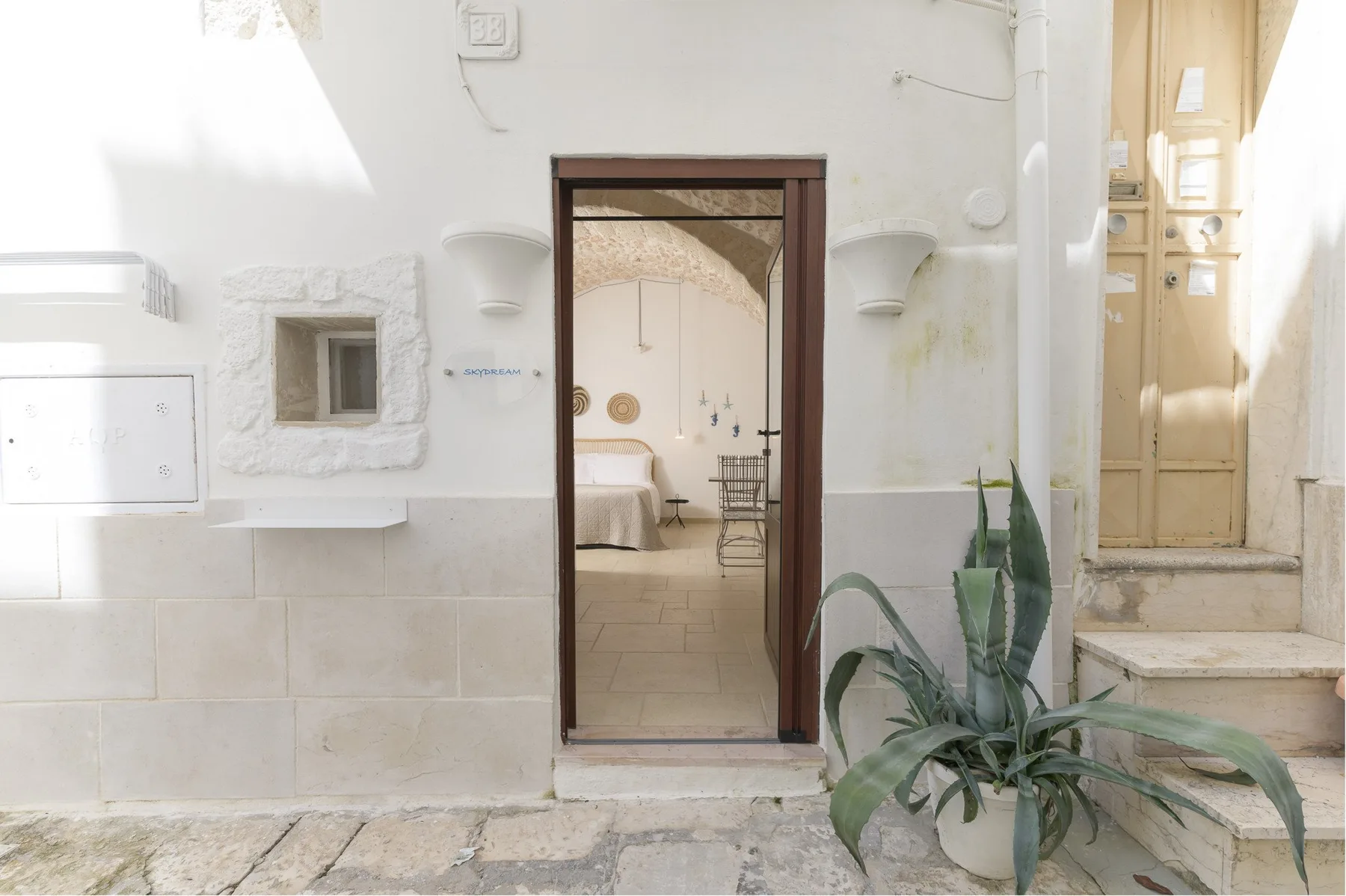 A bedroom is visible through an open doorway, with a bed and a chair.