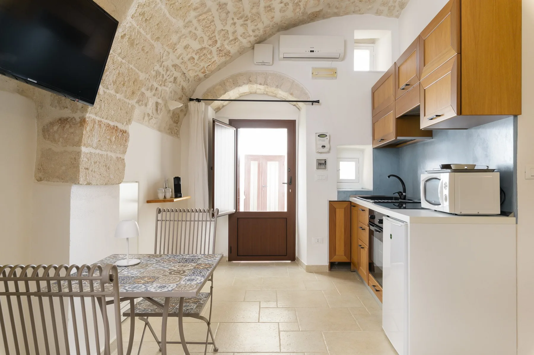 Una pequeña cocina y zona de comedor se encuentra bajo un arco de piedra, con una mesa junto a la puerta.