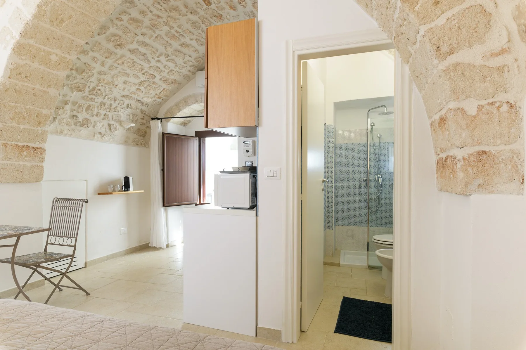 Un interior luminoso muestra un techo abovedado de piedra, una pequeña zona de comedor y la entrada abierta al baño.