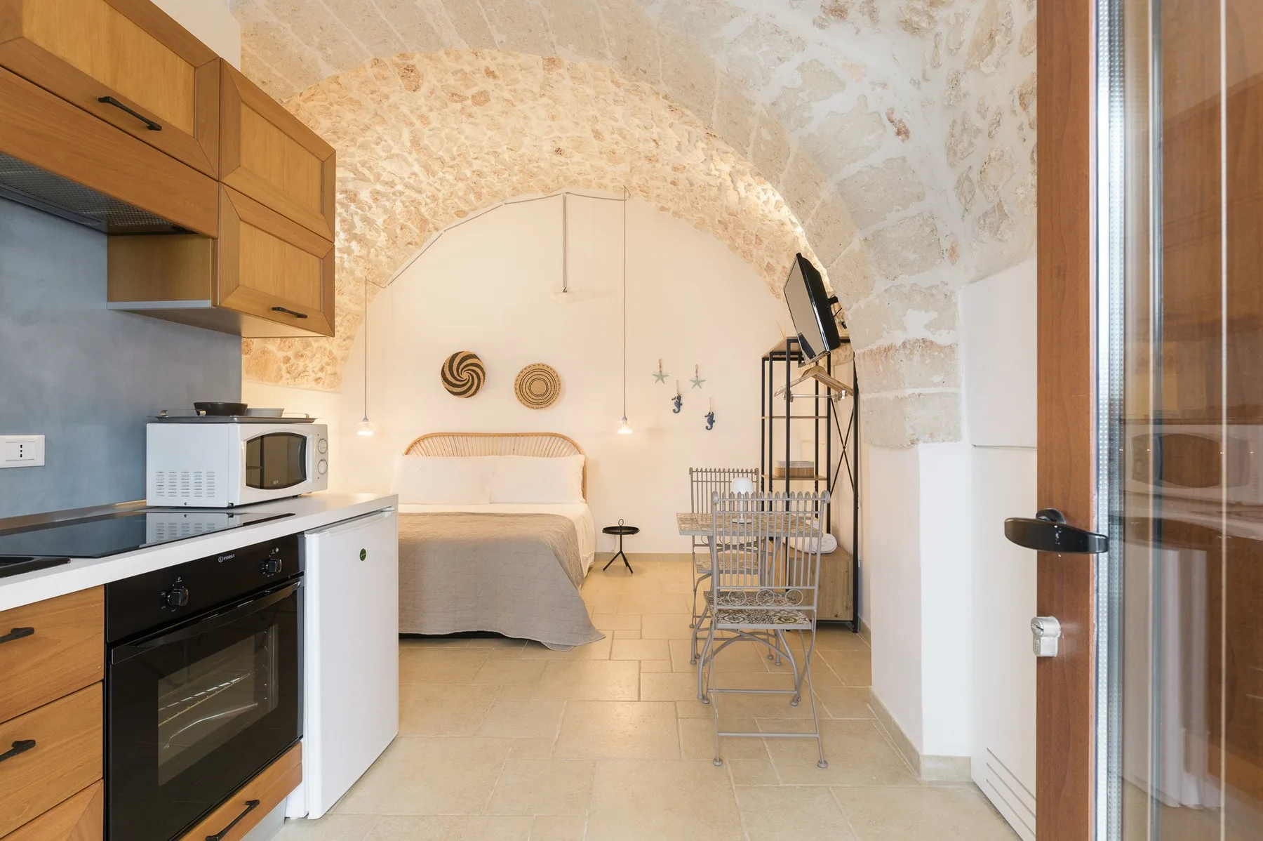 A compact kitchen and sleeping area beneath a stone arch, with a bed and dining chairs.