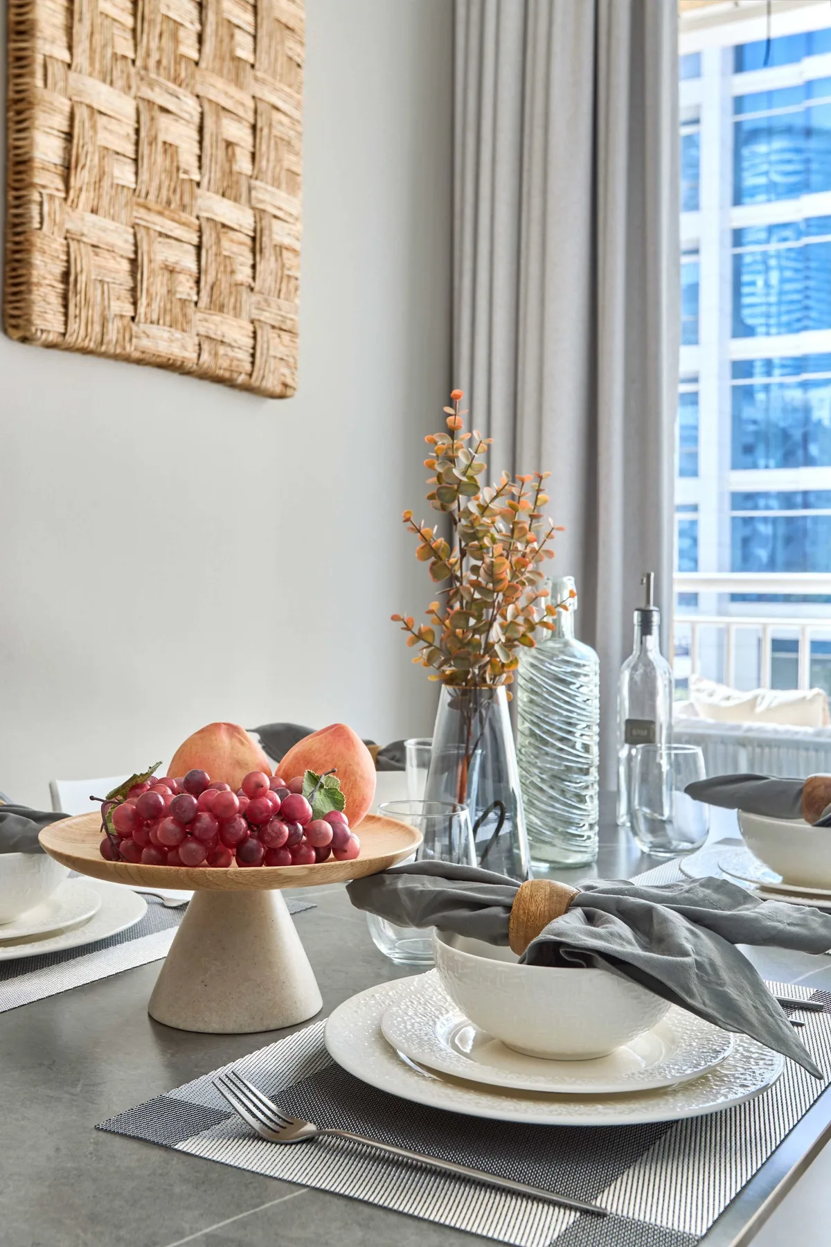 Una mesa de comedor con platos y fruta está junto a una ventana grande.