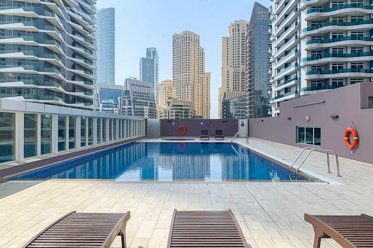 Una piscina al aire libre está en una terraza embaldosada entre edificios altos.
