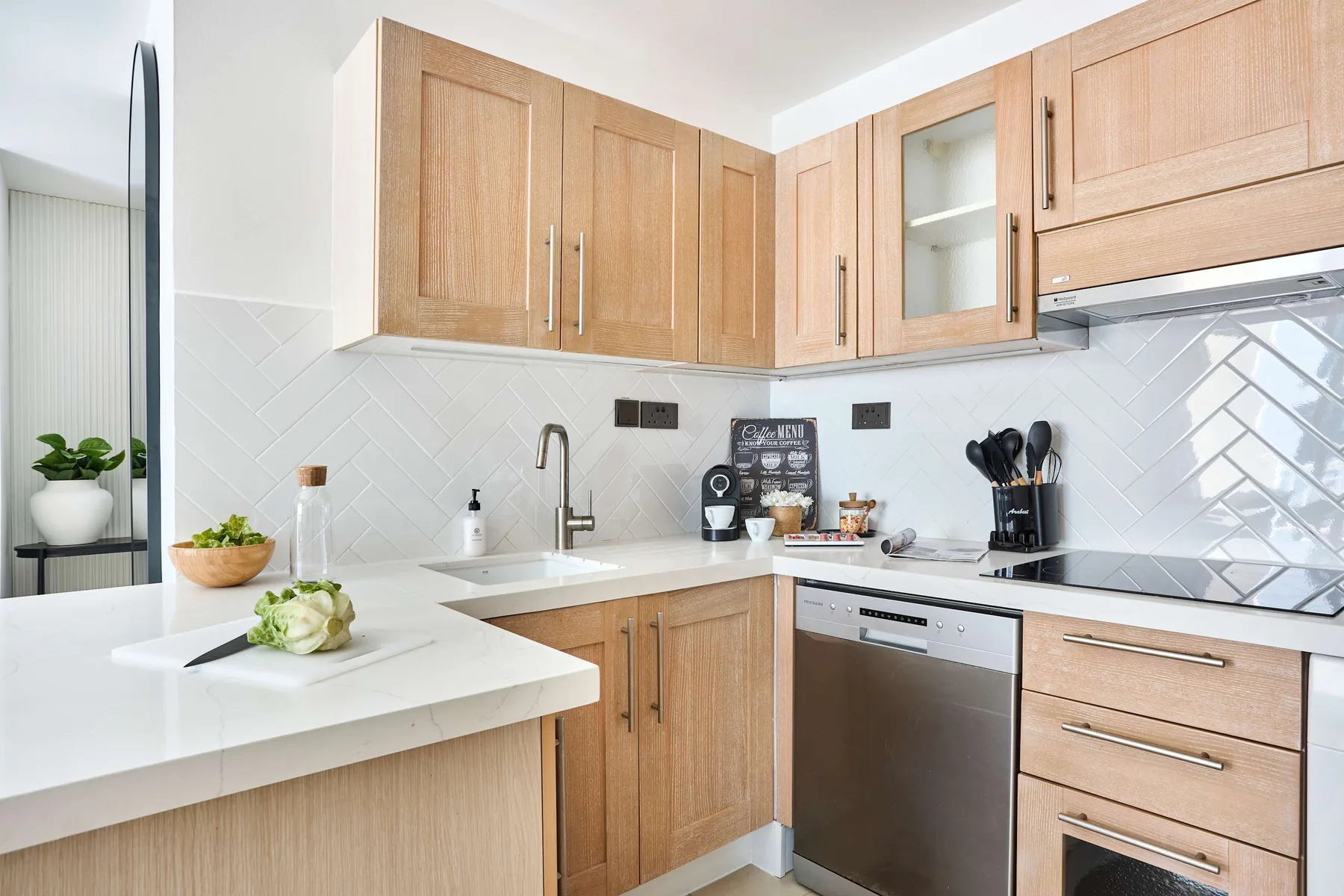 Una cocina luminosa con gabinetes de madera clara, encimeras blancas y un salpicadero de azulejos.