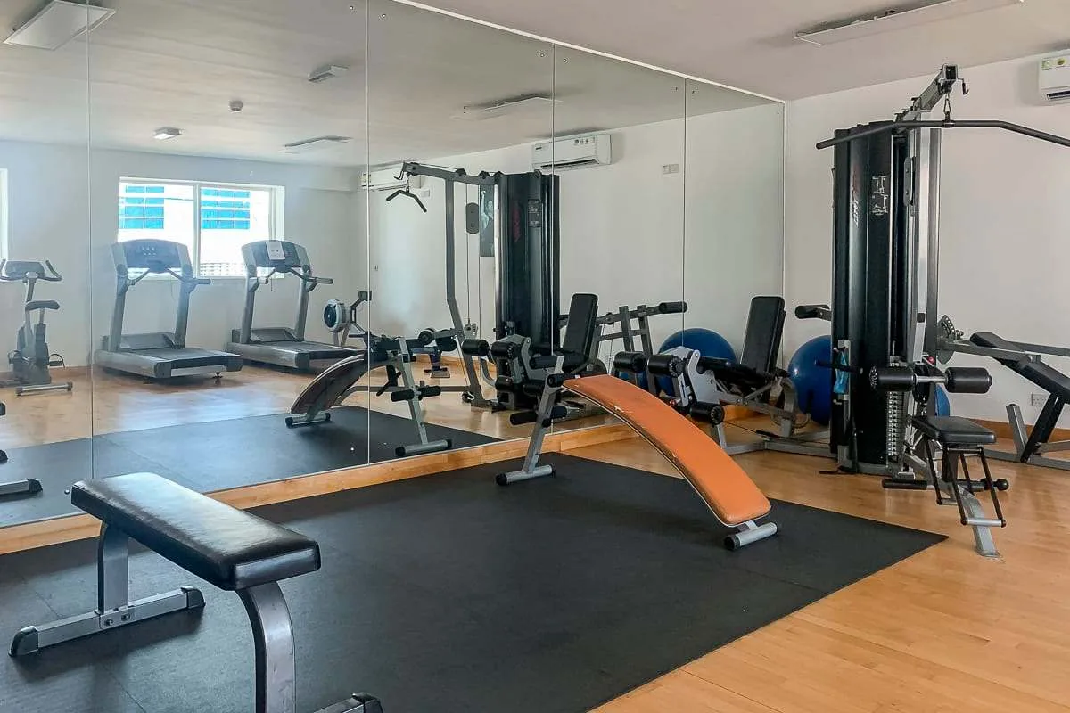 Un gimnasio con máquinas de ejercicio, pesas y un banco frente a una pared con espejos.