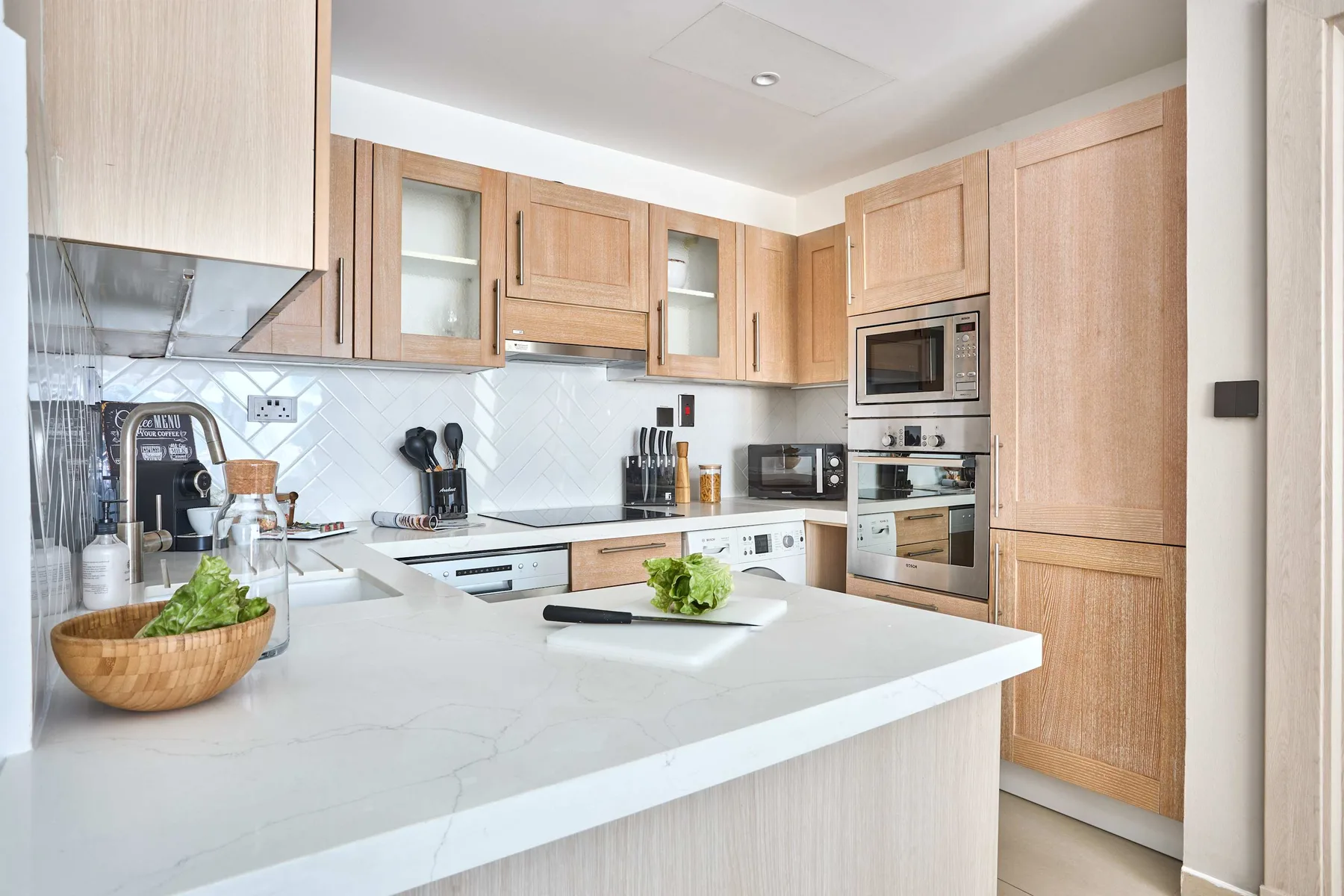 Una cocina luminosa con gabinetes de madera clara y una amplia isla blanca.