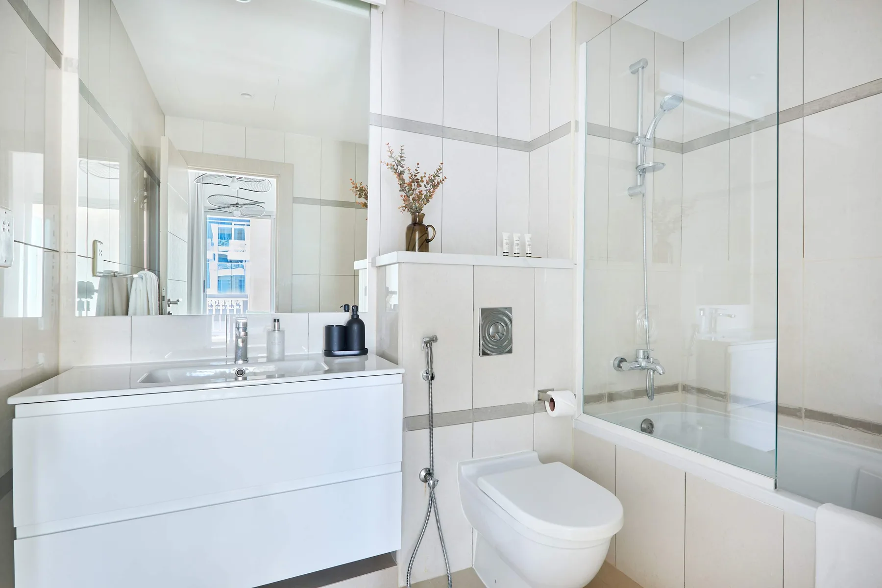 Un baño luminoso con lavabo, inodoro y ducha con mampara de vidrio.