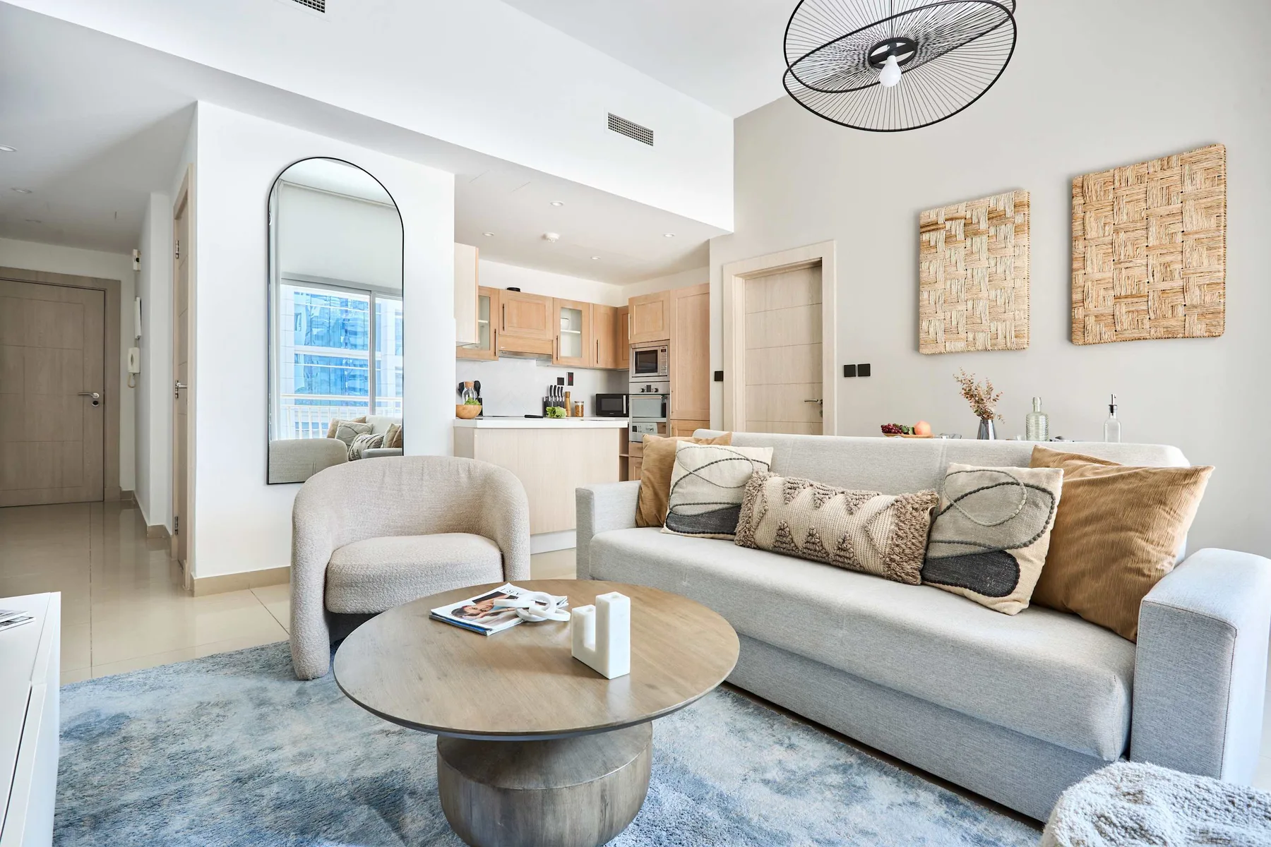 Una sala luminosa con sofá, sillón y cocina abierta al fondo.