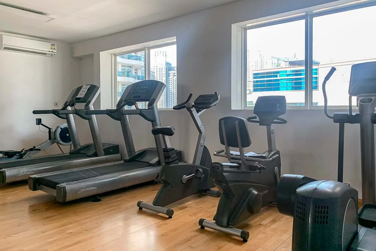 Un gimnasio con máquinas de ejercicio junto a grandes ventanas.