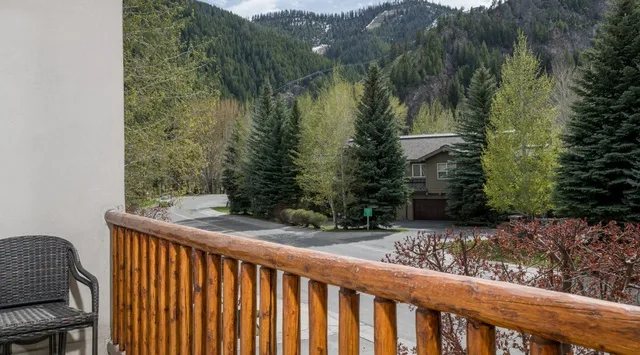 Una barandilla de madera da a árboles, un edificio cercano y montañas boscosas.