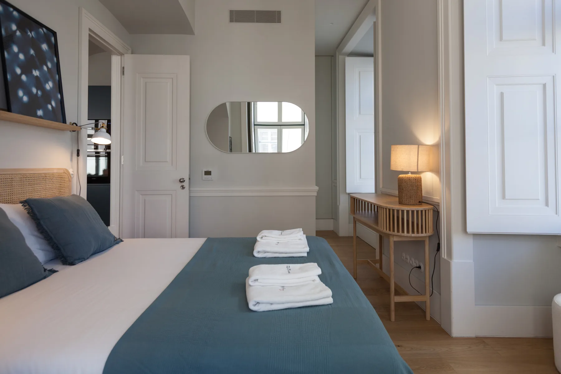Dormitorio con una cama, toallas dobladas y una mesita junto a la ventana.
