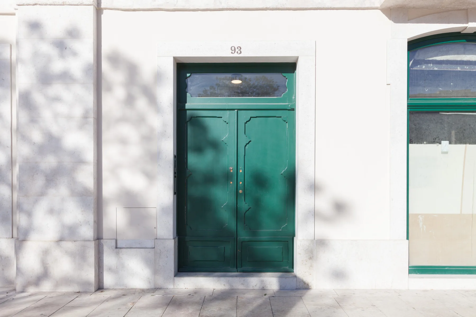 Una puerta verde de dos hojas en una pared exterior blanca.
