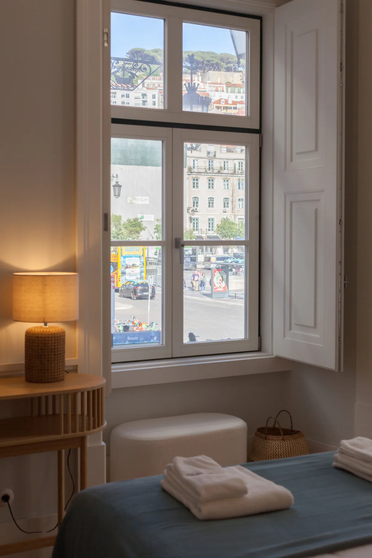 Un dormitorio con una cama, toallas dobladas y una ventana alta con vistas a la calle.