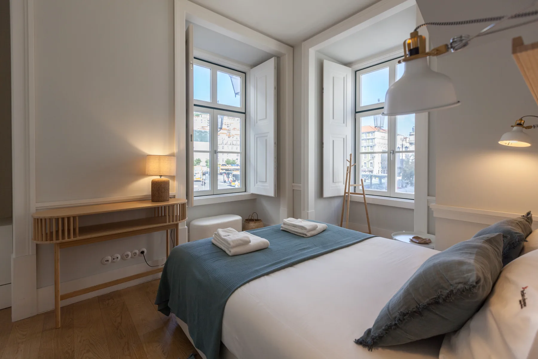 Un dormitorio luminoso con una cama bien hecha junto a ventanas altas.