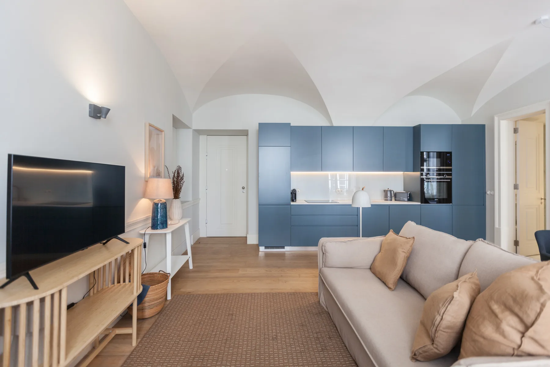 Una sala de estar con televisor, asientos y armarios azules de cocina.