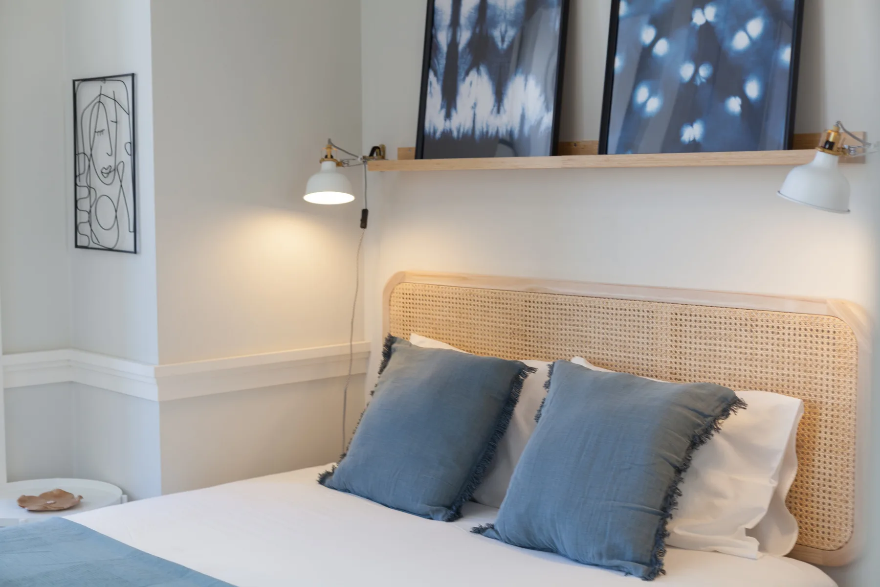 Un dormitorio con una cama, cojines azules y luces de lectura en la pared.